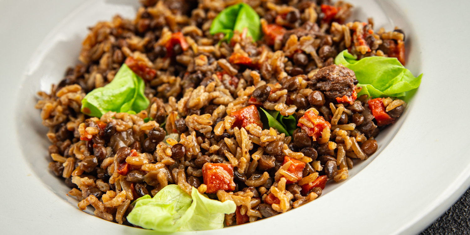 Rice and black beans with diced red peppers and green leaves served on a white plate.