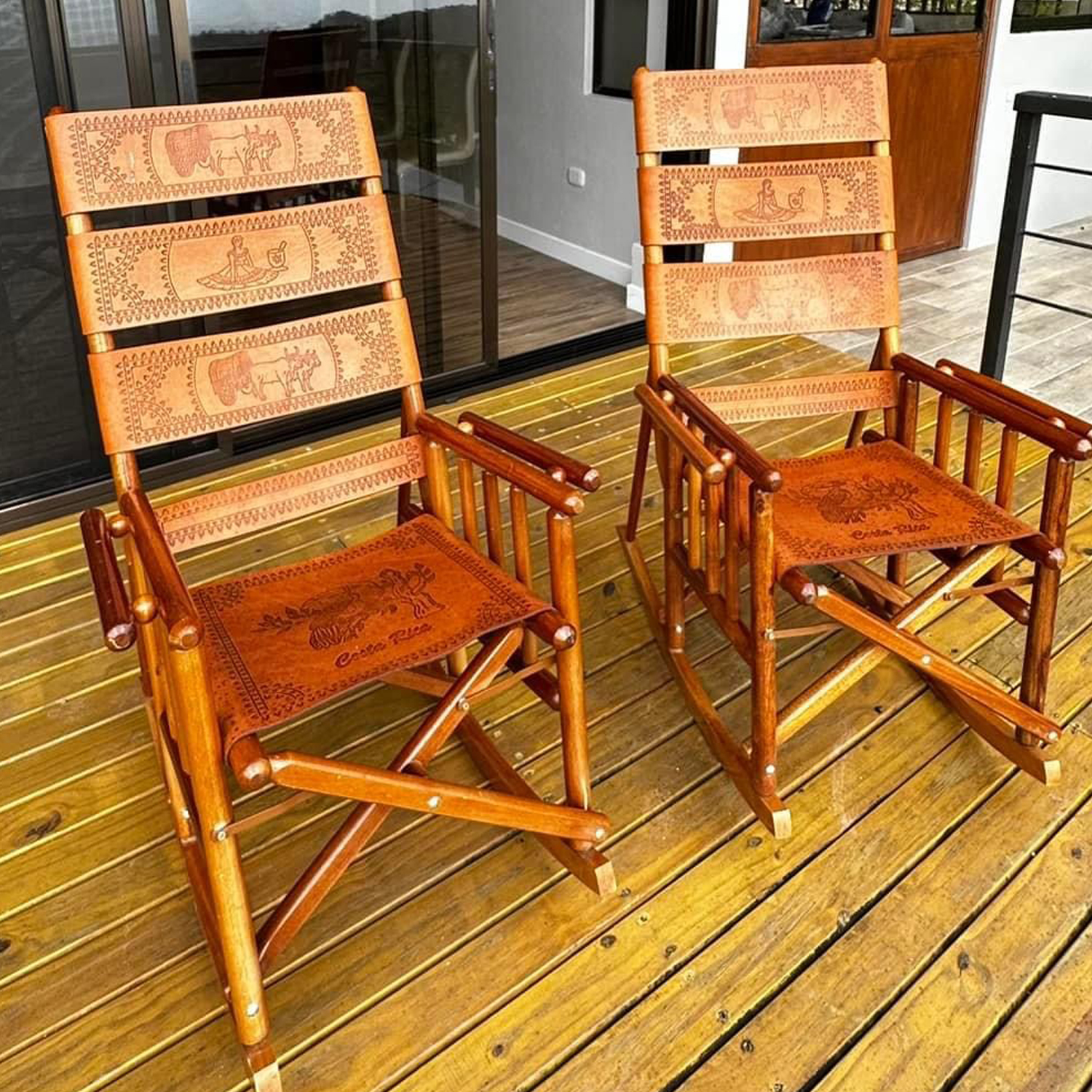 Two wooden rocking chairs with patterned leather seats on a covered wooden deck outside the house.